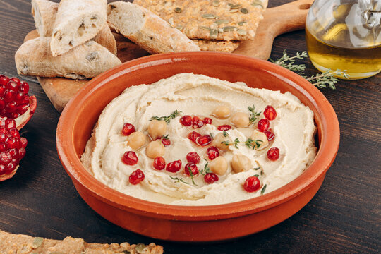 Creamy Hummus With Pomegranate Seeds, Chickpeas, Olive Oil, Pita Bread And Seed Crackers On Wood	