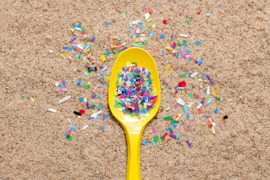 Microplastic in on a plastic spoon. Sandy beach polluted with tiny plastic particles, close up, top view
