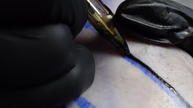 Close-up of a tattoo artist creating a black ink outline over a blue stencil during a tattoo session