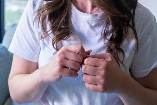 Young woman in a white t-shirt biting and picking at her nails, close-up of anxious hands fidgeting with a nervous habit at home