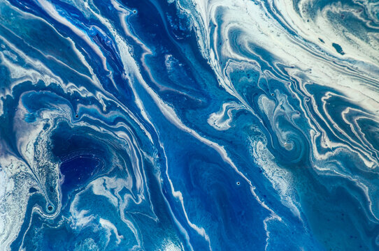 Swirls of blue paint mix on canvas at an art studio