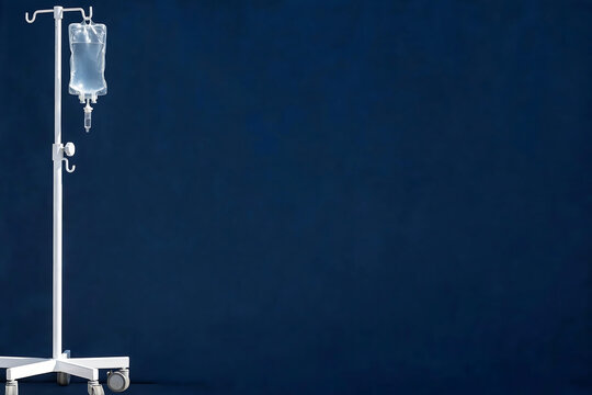 Medical IV drip stand with saline solution bag isolated on a dark blue studio background for healthcare concepts