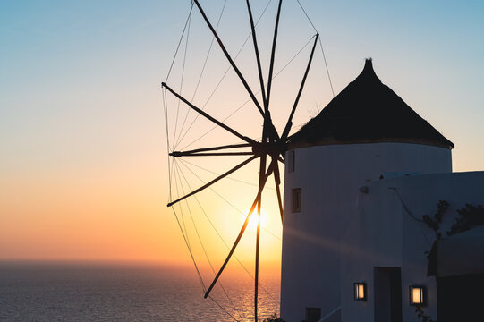 Traditional white windmill in Oia Santorini during a scenic sunset over the Aegean Sea