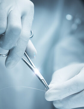 Close up of surgeon hands in sterile medical gloves using stainless steel needle holder and suture
