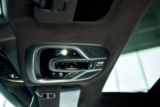 Car interior roof console with hanging key fob and illuminated dome light beside rearview mirror, showing glossy trim, textured upholstery, windshield reflections, and clean modern cabin detail