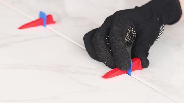 The master uses a plastic wedge and a base (clip) for perfect alignment of porcelain stoneware by level. Tile leveling system in the process of work. Modern auxiliary tools for professional tiling