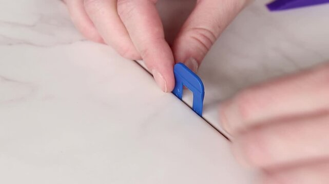 The master uses a plastic wedge and a base (clip) for perfect alignment of porcelain stoneware by level. Tile leveling system in the process of work. Modern auxiliary tools for professional tiling