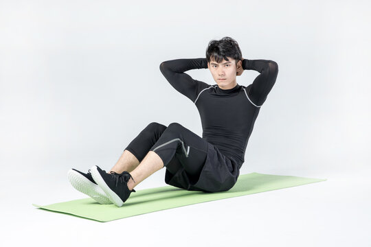 Young man doing sit-up exercise on yoga mat in studio