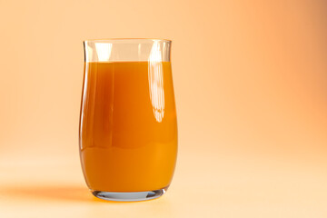 Glass of fresh orange juice on warm peach background © Ruslan