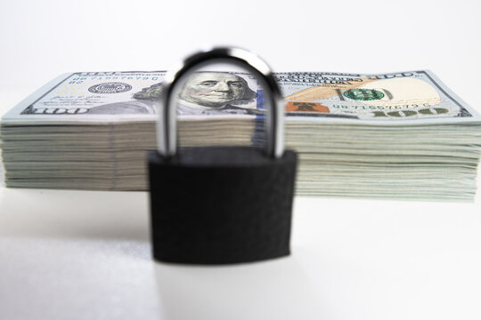 Closed black padlock on stack of US dollar banknotes isolated on white background
