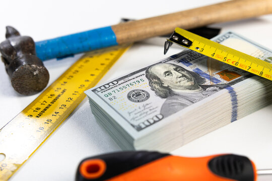 Stack of US dollar banknotes surrounded by construction tools on white background