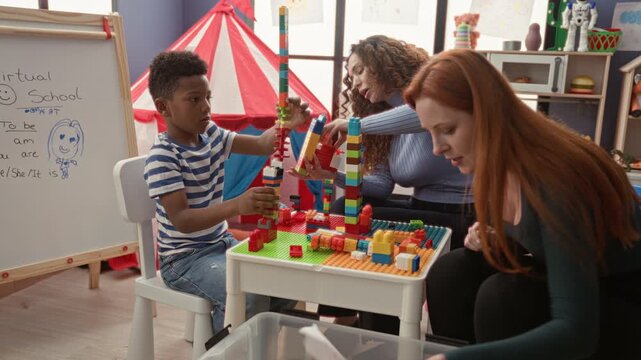 Woman helps boy stack colorful plastic blocks and reaches to place a tower piece in a preschool building; joyful learning.