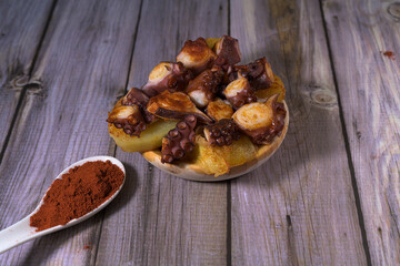 Fototapeta premium Traditional Spanish pulpo a la gallega or octopus with potatoes, paprika and olive oil served on a wooden plate over rustic grey background