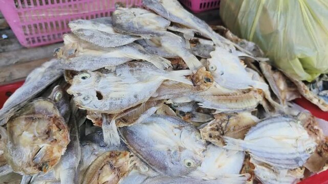 Pile of dried fish for sale at market stall with plastic basket nearby