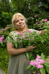 Serene senior woman looking at pink spiraea flower in the garden, cottagecore lifestyle profile portrait © Светлана Высокос
