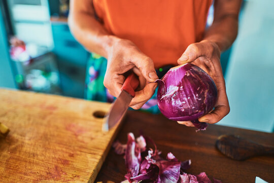 Peeling the skin off a red onion on a chopping board