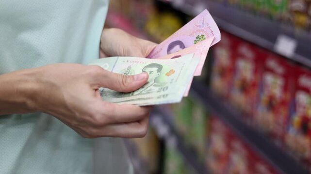 Close up view of woman hands counting cash money (Thai baht banknotes) for shopping in supermarket. Calculating budget to spend in grocery store. Concept of financial planning in Thailand.