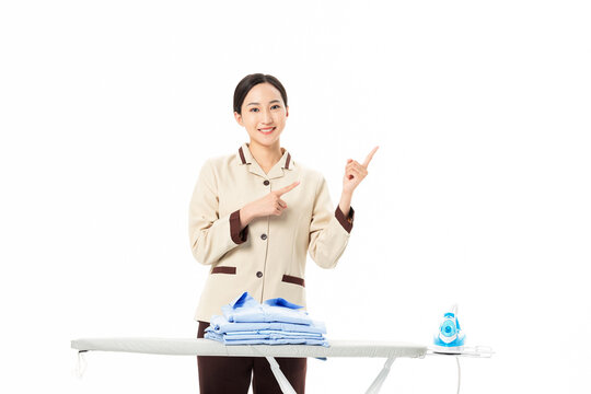 Smiling housekeeper pointing beside ironing board with folded clothes