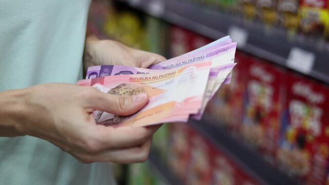 Close up view of woman hands counting cash money (Philippine peso PHP banknotes) for shopping in supermarket. Calculating budget to spend in grocery store. Concept of financial planning in Philippines