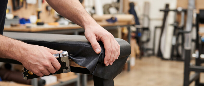 Upholsterer repairing leather bench seat with staple gun in workshop crafting studio