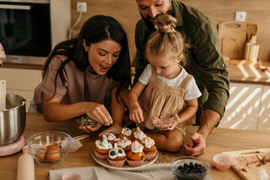 Happy family decorating cupcakes with sprinkles in kitchen