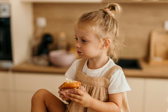 Cute little girl eating sweet muffin in kitchen