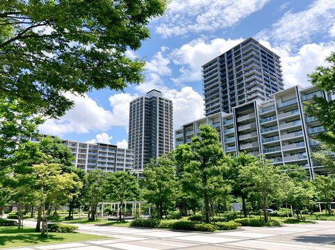 青空と豊かな緑に囲まれた公園の奥にそびえ立つ高層タワーマンションの風景