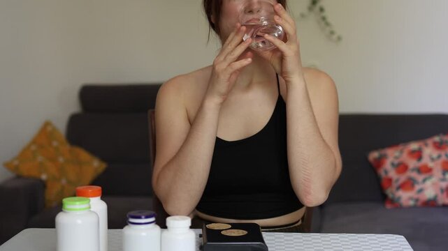 Young woman takes pill with water at home showing mindful approach to health routine and conscious supplement use as part of daily self care habit