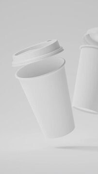 Two minimalist white blank takeaway coffee cups floating above a white background in a seamless 3D loop. Vertical video.