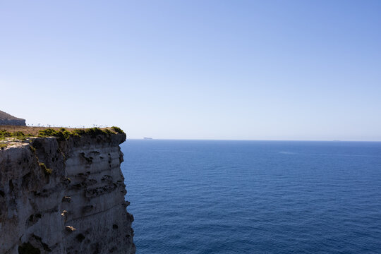 High steep rocky cliff edge next to the endless blue mediterranean sea in Malta.