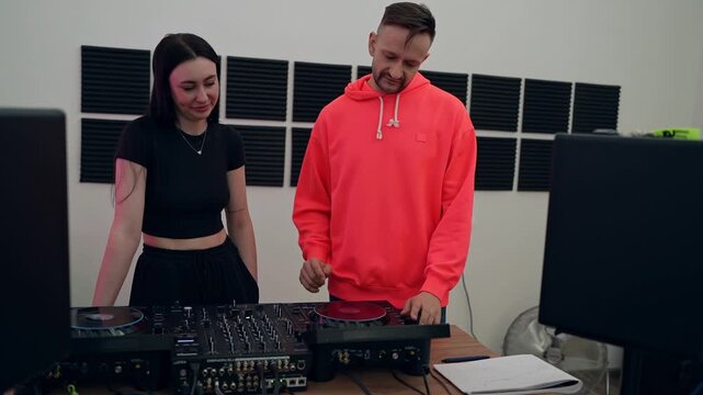 DJ instructor working closely with female student demonstrating mixer controls at studio desk. DJ, instructor, mixer, controls, demonstration, studio