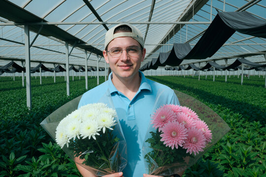 Portrait of young adult Caucasian man holding flower bouquets in greenhouse, presenting commercial floriculture production and fresh cut blooms for retail marketing and agriculture