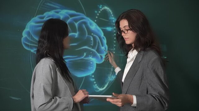 Two women discuss brain science with a digital graphic in a classroom setting