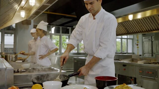 Chef cooks in a busy kitchen while other staff prepare dishes and manage tasks during the lunchtime rush