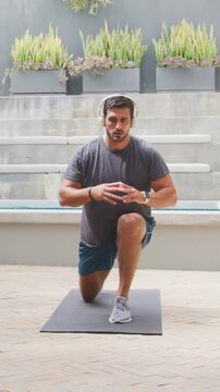 Vertical video: Stepping onto mat, man doing lunges with knee lifts on patio, in shorts for fitness