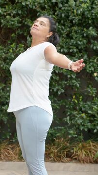 Vertical video: Breathing deep woman in white tee blue pants opening arms on patio, watch bracelets