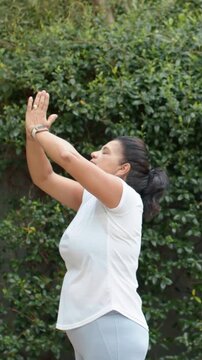 Vertical video: Upward reaching woman lowering hands into prayer at hedge in gear with watch calmly