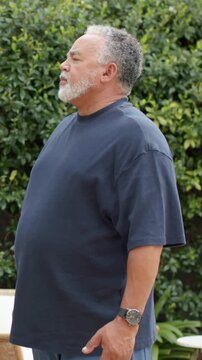 Vertical video: Starting upright mature man in navy tee stretching arms on patio, breathing