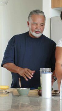 Vertical video: Pointing man in navy T guiding her fitting blender cup lid on kitchen bar for drink