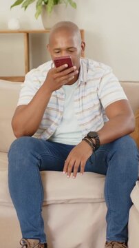 Vertical video: Holding maroon phone to mouth, man wearing striped shirt and watch speaking at home