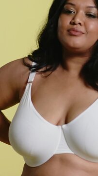 Vertical video: Camera moving in, model shifting side to front at yellow set, posing in white bra