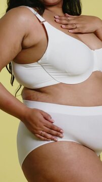 Vertical video: Camera panning model smoothing briefs adjusting underwire bra showing fit in studio