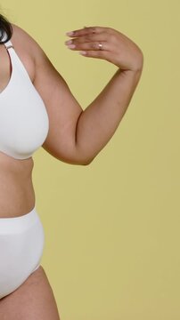 Vertical video: Moving hand, model extending arm, rotating at yellow studio showing white lingerie
