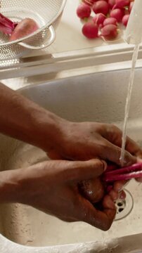 Vertical video: Rinsing hands trimming radish under running faucet at kitchen sink, removing dirt