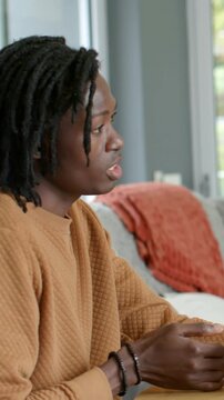 Vertical video: Holding cup, dreadlocked man in mustard top responding to offscreen cue at table