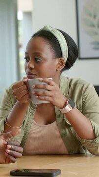 Vertical video: Holding woman wearing green headband sipping grey mug at home, responding to hands