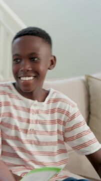 Vertical video: Smiling kid reaching, showing green folder on couch, turning pages after adult cue