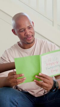 Vertical video: Giving lime card, son urging father pink tee home reading Happy Fathers Day hugging