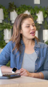 Vertical video: Hearing coworker speak, woman in denim top gesturing, speaking at table with laptop