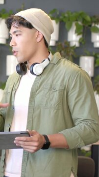 Vertical video: Holding tablet, man in beanie tapping screen in workspace, demoing to peer entering